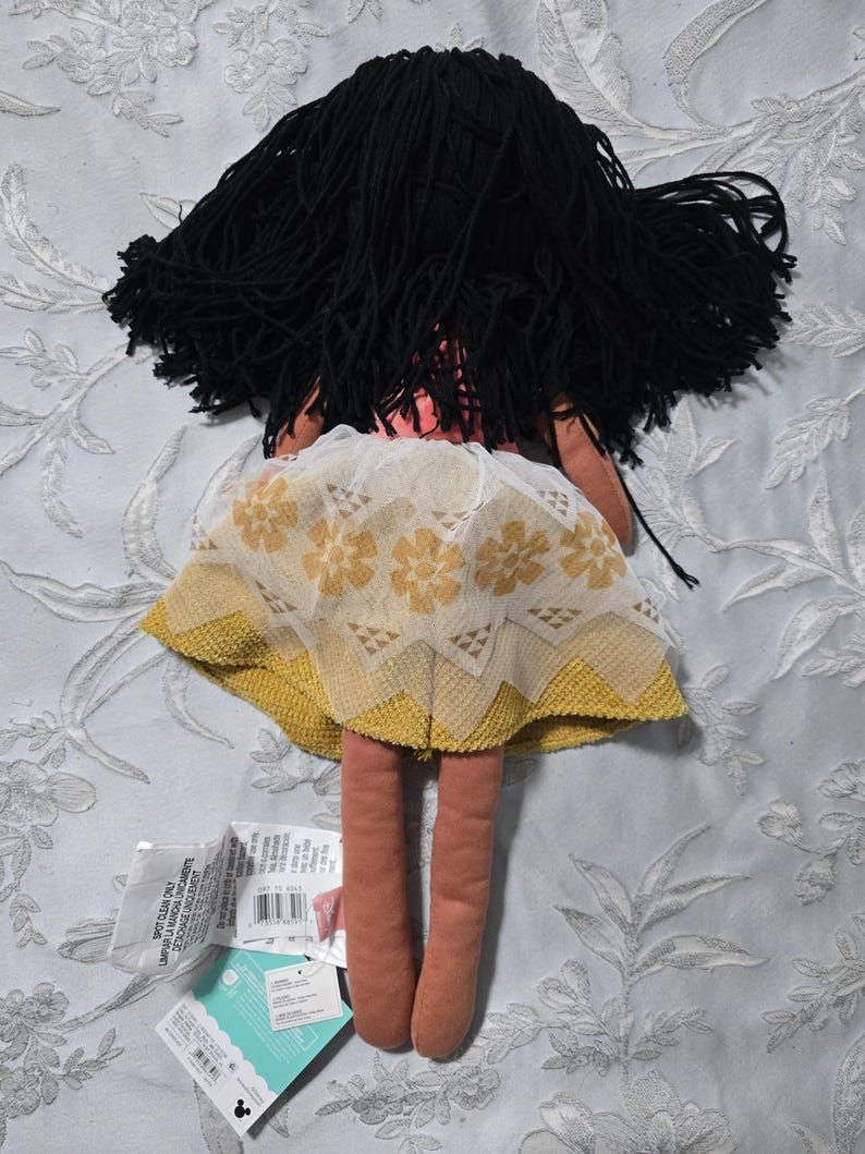 May include: A handmade doll with black yarn hair and a yellow and white floral skirt. The doll has long, slender legs and a pink torso. Tags are attached to the doll.