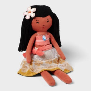 May include: A plush doll with black yarn hair, a pink flower, and a coral-colored top and skirt. The doll has a necklace with a blue pendant and a white and gold patterned skirt. The doll is sitting down.