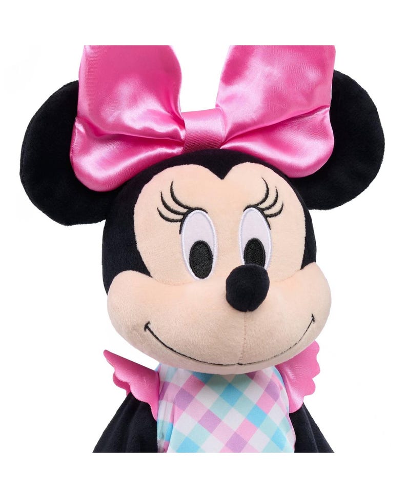 May include: A plush Minnie Mouse doll with black ears and a large pink satin bow. The doll has a light pink face, black eyes, and a black nose. She wears a dress with a pastel plaid pattern and pink ruffled sleeves.