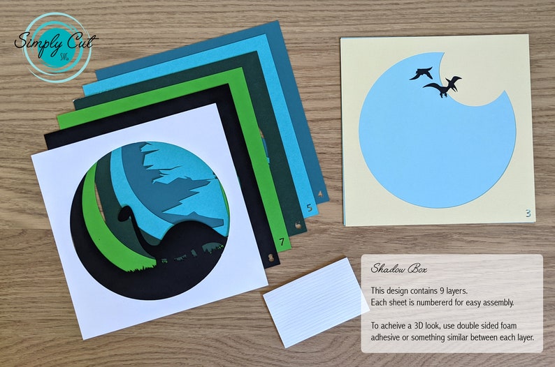 May include: A 9-layer papercraft shadow box kit featuring a dinosaur silhouette with a green, blue, and black colour scheme. The kit includes instructions for assembly and a note about using double-sided foam adhesive for a 3D effect.
