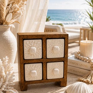 May include: A small wooden storage chest featuring four square drawers with white ceramic fronts. Each drawer face displays a unique embossed pattern and a small, centred square knob. The frame is constructed from dark brown wood.