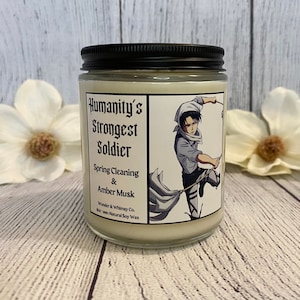 May include: A white candle jar with a black lid and a label that reads "Humanity's Strongest Soldier Spring Cleaning & Amber Musk" with an anime character on the label. The candle is made with natural soy wax.