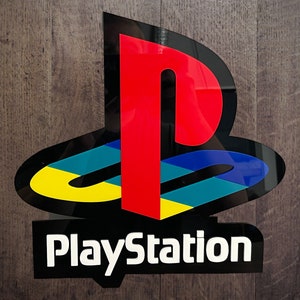 May include: A black and white PlayStation logo with a red, blue, and yellow circle design. The text "PlayStation" is written in white letters below the logo.