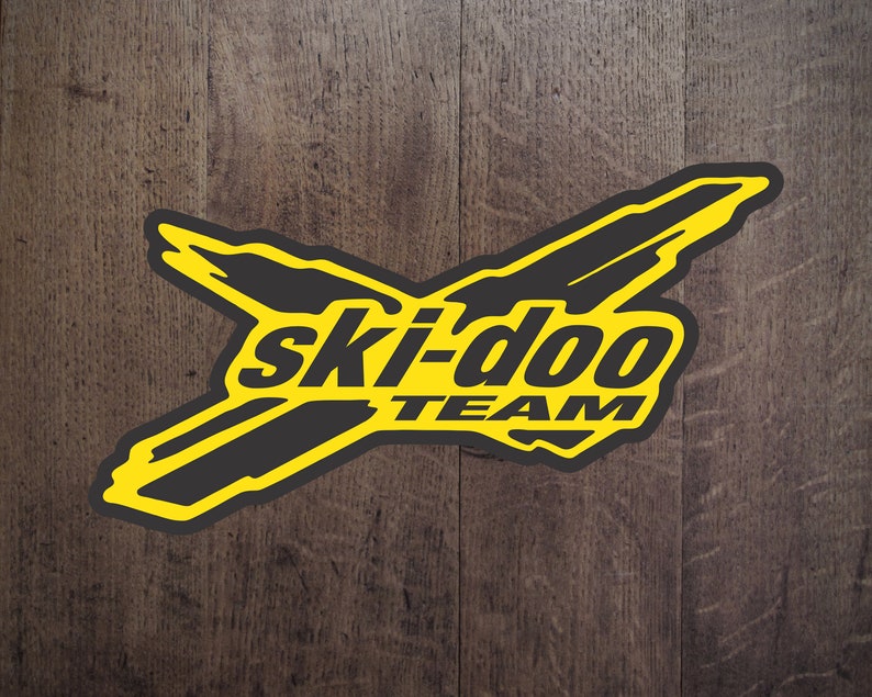 May include: A yellow and black logo with the text "ski-doo team" on a wooden background.