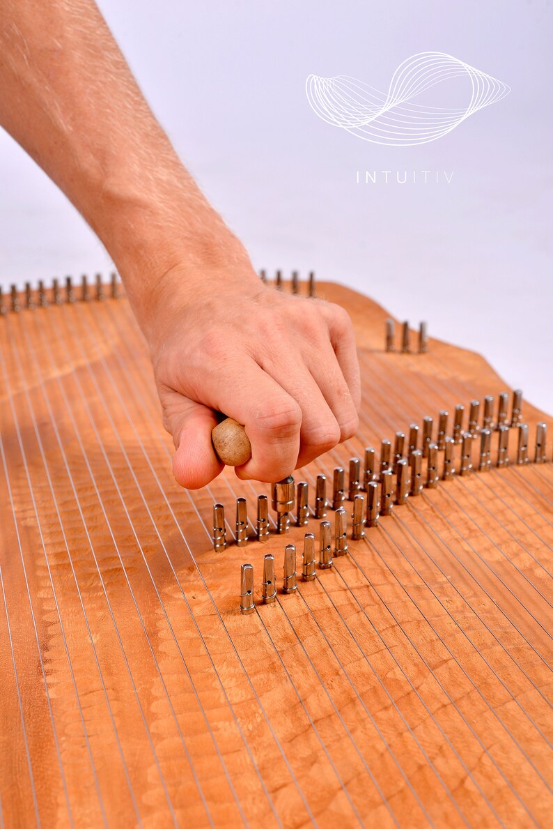 May include: A wooden musical instrument with metal pins and strings. A hand is holding a wooden mallet and striking the pins.