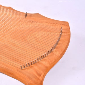 May include: A wooden lyre with a curved shape and many strings. The lyre is made of light wood with a natural grain pattern. The strings are attached to metal tuning pegs.