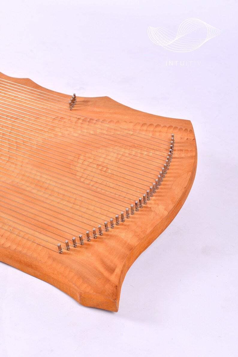 May include: A wooden lyre with a curved shape and many strings. The lyre is made of light wood with a natural grain pattern. The strings are attached to metal tuning pegs.