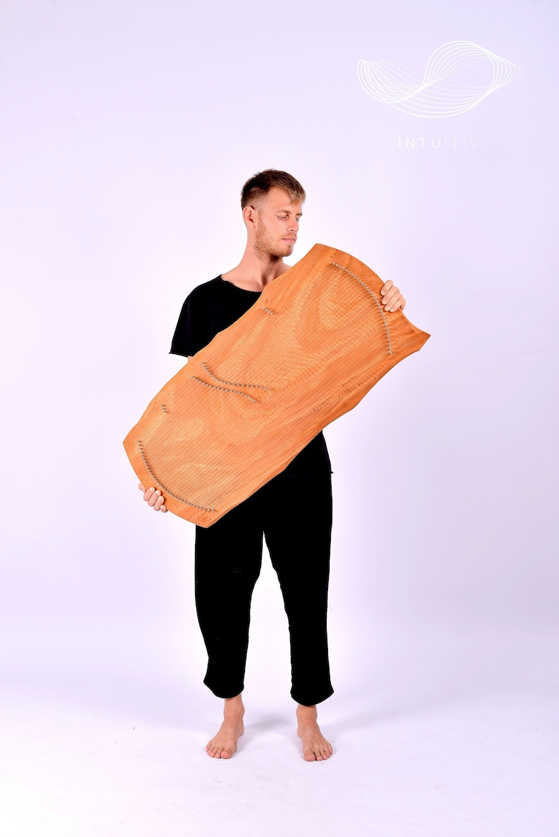 May include: A person holding a wooden musical instrument with metal pins. The instrument is brown and has a natural wood grain. The person is wearing black pants and a black shirt.
