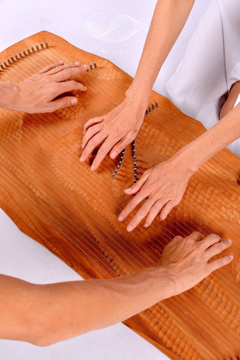 May include: Two people playing a wooden musical instrument called a  'Lyre' or 'Harp' with strings. The instrument has a natural wood finish and is decorated with intricate carvings. The word 'INTUITIV' is visible on the instrument.
