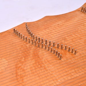 May include: A wooden musical instrument with a curved shape and multiple strings. The instrument has metal tuning pegs along the top edge.