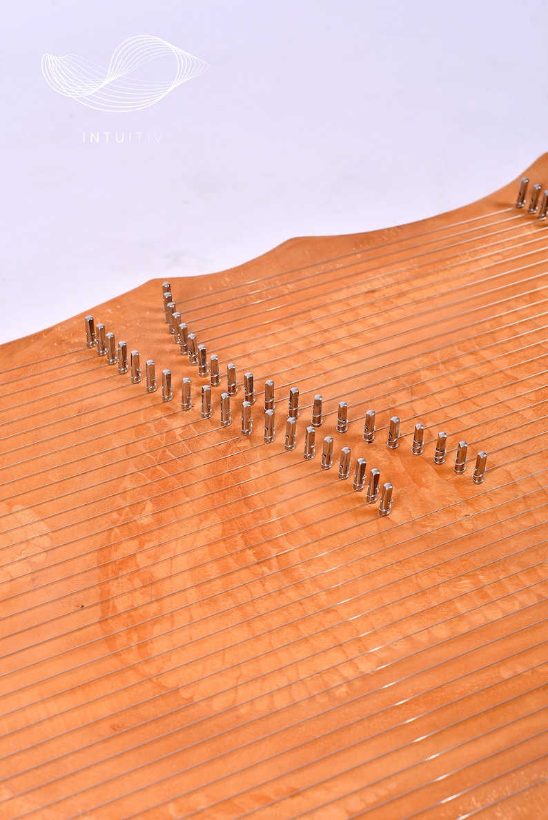 May include: A wooden musical instrument with a curved shape and multiple strings. The instrument has metal tuning pegs along the top edge.