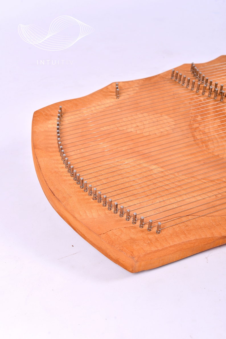 May include: A wooden lyre with a curved shape and multiple strings attached to metal tuning pegs. The lyre is made of light wood with a natural finish.