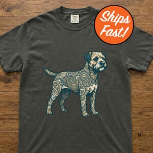 May include: A charcoal gray short-sleeve t-shirt featuring a graphic of a standing dog. The dog is filled with a detailed, intricate paisley pattern in shades of cream, light blue, and dark blue. The shirt has a crew neckline and a tag.