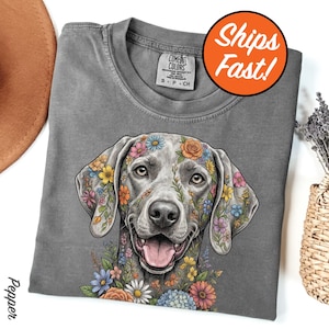 May include: A gray Comfort Colors t-shirt featuring a smiling dog with colorful floral designs on its face and ears. The shirt has a crew neck and short sleeves. The text "Ships Fast!" is in a circle on the upper right.
