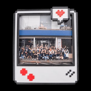 May include: A white and black framed photo with a pixelated design. The photo features a group of people with their arms raised. Red pixelated hearts and buttons are on the frame, with a pixelated speech bubble.