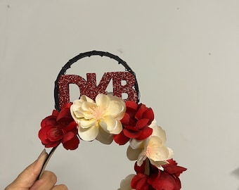 May include: A red and white floral headband with the letters "DKB" in red glitter on a black wire frame.