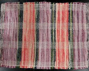 May include: A woven rug with a striped pattern in shades of pink, red, white, green, and purple.
