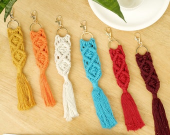 May include: Seven colorful macrame keychains with gold rings. The keychains are made with a variety of colors, including blue, red, white, orange, and brown.