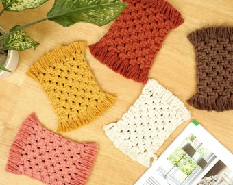 May include: Four handmade macrame coasters in different colors: brown, white, yellow, and pink. Each coaster has a square shape with fringed edges.