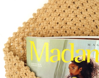 May include: A tan crocheted wall hanging with a magazine titled "Madan" on top. The magazine cover features a woman with long dark hair and a yellow top.