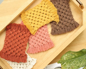 May include: Four crocheted coasters in a wooden tray. The coasters are in shades of brown, pink, yellow, and white with fringe detailing.