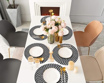 May include: A set of five black and white woven placemats with a geometric pattern. The placemats are arranged on a white table with white plates and gold silverware.