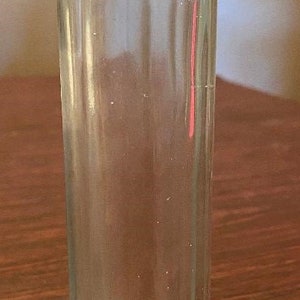 May include: A clear glass bottle with a textured surface. The bottle has a rounded top and a straight, cylindrical body.