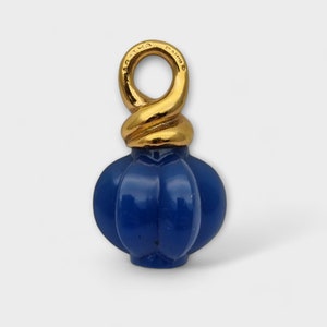 Könnte beinhalten: Ein blauer Glasanhänger mit einer goldenen Metallslaufe und der Aufschrift "PAT.MA. CAD.NO. 5".