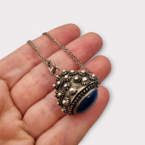 Può includere: Collana con pendente argentato con un pendente rotondo strutturato e una pietra blu scuro. Il pendente è adornato con piccoli dettagli a forma di fiore e pende da una delicata catena. Stile vintage.