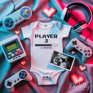 May include: A white baby onesie with the text "PLAYER 3 LOADING..." in black pixelated font. The onesie is surrounded by video game controllers, a pair of headphones, and pixelated hearts.