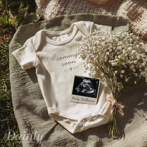 May include: Cream-colored baby onesie with the words "coming soon" and the month and year printed on it. A sonogram photo and a bouquet of white flowers are next to the onesie. The sonogram photo has the name "Baby Williams" printed on it.