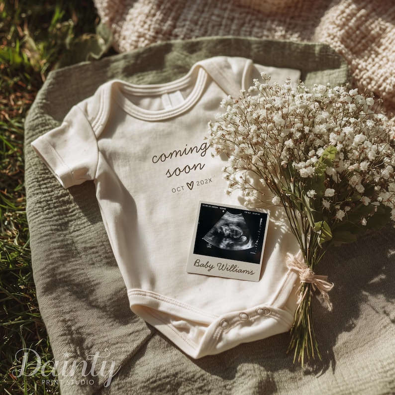 May include: Cream-colored baby onesie with the words "coming soon" and the month and year printed on it. A sonogram photo and a bouquet of white flowers are next to the onesie. The sonogram photo has the name "Baby Williams" printed on it.