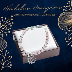 May include: A crystal, rhinestone, and CZ bracelet with a silver charm in a brown box. The bracelet is made of clear and pink beads. The charm is a star-shaped symbol.