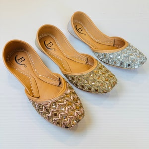 May include: Three pairs of flat shoes with intricate embroidery and mirrored embellishments. The shoes are in shades of silver, gold, and rose gold. The shoes have a pointed toe and a low heel. The brand name "B" is visible on the insole of each shoe.