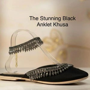 May include: Black Khusa flat with beaded ankle strap. The shoe features a pointed toe and a decorative beaded trim. The text on the image reads "The Stunning Black Anklet Khusa."