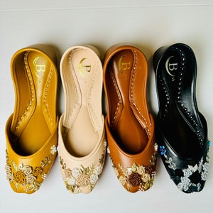 May include: Three pairs of flat shoes with embroidered floral designs. The shoes are in black, brown, and beige.