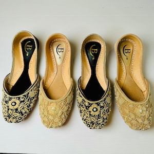 May include: Four pairs of gold and black embroidered flat shoes with a pointed toe. The shoes have a black velvet lining and are decorated with gold thread and pearls.