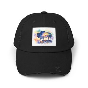 May include: A black distressed baseball cap featuring a rectangular graphic print on the front panel. The print displays a silhouette of a bison against a vibrant, multicolored watercolor background with a bright sunburst and starry night sky.