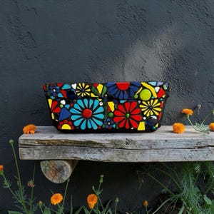 May include: A rectangular planter decorated with a vibrant mosaic pattern of multi-coloured glass tiles. The design features stylised flower shapes in bright shades of red, blue, yellow, and green against a dark grout background.