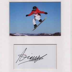 Può includere: Fotografia incorniciata di uno snowboarder a mezz'aria contro un cielo blu e montagne innevate. Lo snowboarder indossa una giacca rossa, pantaloni bianchi e un casco nero. Sotto, un passe-partout bianco con una firma nera.