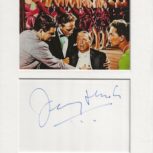 May include: A black and white photograph of a man in a suit with a group of women in the background. The man is looking at the camera and the women are looking away. The man's signature is written in blue ink below the photo.