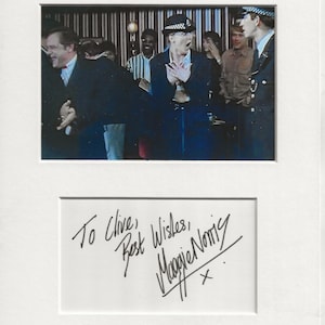 Puede incluir: Una fotografía en blanco y negro de un grupo de personas, incluyendo un hombre con uniforme de policía, con un autógrafo de Maggie Norris que dice "To Clive, Best Wishes, Maggie Norris".