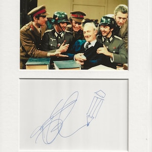 Könnte beinhalten: Ein Schwarzweißfoto einer Gruppe von Männern in Militäruniform. Die Männer lächeln und scheinen gute Laune zu haben. Das Foto ist von einem der Männer signiert, mit einer Bleistiftzeichnung eines Bleistifts neben der Unterschrift.