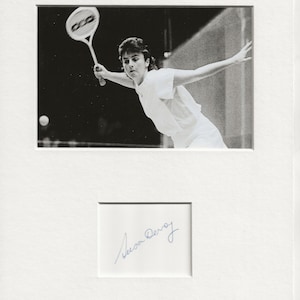 Pode incluir: Fotografia a preto e branco de uma mulher a jogar squash. Ela está vestida com uma camisa e calções brancos e está a balançar a sua raquete. A fotografia está assinada "Susan Devoy".