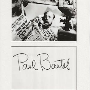 May include: Black and white photo of Paul Bartel, an American actor and filmmaker, on a phone. He is holding a newspaper with the headline "DOGS TEAR UP NEWBORN BABY".