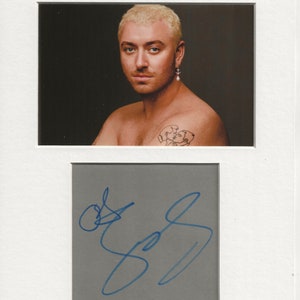 Könnte beinhalten: Ein Schwarzweißfoto eines Mannes mit blonden Haaren und einem Tattoo auf der Schulter. Der Mann schaut in die Kamera. Das Foto ist mit blauer Tinte signiert.