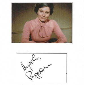 May include: A vintage photograph featuring a woman in a pink blouse with a bow detail. The image includes an autograph in black ink on a white background. The woman has dark hair and is seated, with a neutral background.