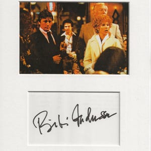 May include: A black and white signed photograph of actress Bibi Andersson. The photo shows Andersson with other actors in a scene from a film.