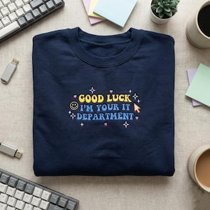 May include: Navy blue sweatshirt with the text "GOOD LUCK I'M YOUR IT DEPARTMENT" in yellow, blue, and white. The design includes a smiling face, stars, and a computer cursor. A casual, comfortable top.