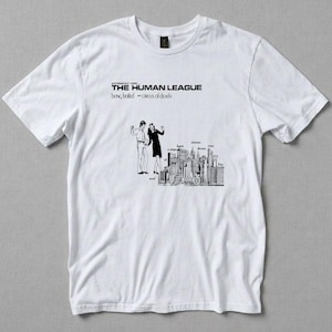 Puede incluir: Camiseta blanca con un diseño en blanco y negro. El diseño incluye el texto "THE HUMAN LEAGUE" y "being boiled - circus of death", junto con una ilustración de dos personas y un horizonte urbano.